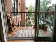 Narrow brick walk-up balcony floored in interlocking wood deck tiles with a striped rug and a folded chair
