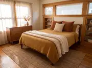 Queen bed layered with a mustard waffle-weave coverlet, rust corduroy pillows, and a folded cream knit blanket