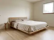 Low ash platform bed with a slatted headboard and oatmeal linen bedding in a bare, warm-white room