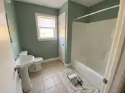 Small bathroom with sage green walls, a white pedestal sink, and a paint roller tray on a drop cloth by the tub