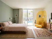 Palm Springs bedroom with a sage wall, mustard Togo chair, potted cacti, and sliding doors to a pool and desert mountains