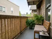 Long balcony railing wrapped in a natural bamboo reed screen beside a cushioned bench and a potted fern