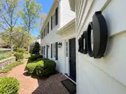 Oversized matte black house numerals mounted on white siding beside a navy door and black lanterns