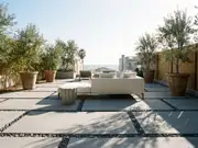 Outdoor lounge patio with a beige sectional on a dark rug over stone pavers, large clay planters, and a wooden fence