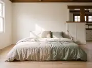 Wrinkled oatmeal and sage linen bedding layered with one nubby woven cushion on a low bed