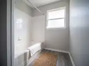 Hall bathroom with a refinished glossy white tub and square tile surround, gray walls, and a jute bath mat