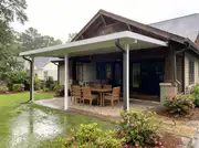 White insulated panel roof attached to a craftsman house keeping a paver dining set dry in the rain