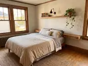 Floating wood shelf headboard with a stack of books, a black wall sconce, and a trailing plant above a neutrally dressed bed
