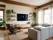Wall-mounted TV flanked by two wooden floating shelves holding plants and books, above a grey sectional by a window