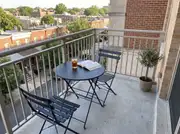 Round black bistro table with two folding chairs, iced tea and a book on a concrete balcony with an olive tree