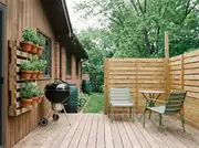 Wall-mounted pallet planter with potted herbs beside a black kettle grill on a wood deck, a slatted privacy screen behind