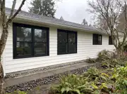A ranch house facade with large windows freshly trimmed in matte black against light siding