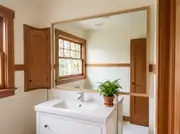Large oak-framed mirror spanning a white vanity in a craftsman bathroom, reflecting a window and fir trim