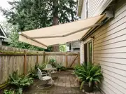 Cream retractable awning cranked out from a bungalow wall over a small paver patio with a bistro set