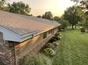 A close-up ranch house roofline with freshly painted light-colored fascia and matching gutters