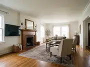 A wall-mounted TV positioned beside a brick fireplace mantel styled with a mirror and candles
