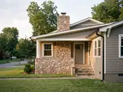 Gray lap-sided house where a natural stone porch base and chimney are the only textured material