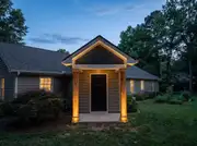 A ranch house entry with a new gabled portico on two wood columns sheltering the front door at dusk