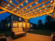 Globe string lights zigzagged across timber pergola rafters, glowing against a deep blue dusk sky