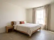 Single terracotta accent pillow on white linen bedding in an otherwise neutral oatmeal bedroom