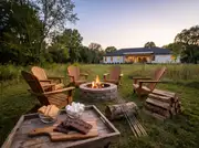 Stone fire pit ringed by four Adirondack chairs with a tray of graham crackers, marshmallows and chocolate beside it