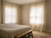 Floor-length cotton-gauze curtain panels filtering late-morning sun across a linen-dressed bed