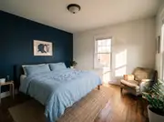 Deep navy accent wall behind a bed with light blue bedding and a single framed abstract print centered above