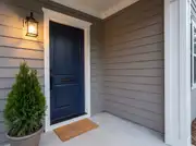 Navy front door with a matte black handle set, mail slot and glowing lantern on warm gray siding