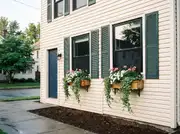 Cream vinyl-sided house with two cedar window boxes of white petunias, pink geraniums and trailing ivy