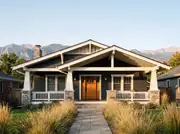 Charcoal craftsman bungalow with tapered white porch columns on stone piers and a wood front door