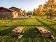 Two cornhole boards, a ladder toss and a roundnet set on a lawn, set well away from a buffet table in the distance