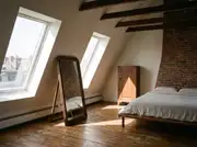 Small attic bedroom with a tall floor mirror leaning against the wall beside a window