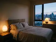 Paper-shade bedside lamp and a ceramic dresser lamp lighting a bedroom at dusk with the overhead off
