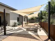 Three cream triangular shade sails overlapping at different heights above a gravel and concrete patio