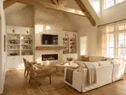 Wall-mounted TV above a lit stone fireplace, flanked by built-in white shelves, with a beige sectional by curtained windows