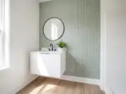Green and white geometric peel-and-stick wallpaper on one wall behind a white floating vanity and round mirror