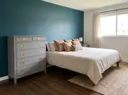Newly repainted matte grey five-drawer dresser with brass knobs standing against a teal accent wall