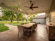 Long wood dining table for eight under a covered patio roof with a wide-blade ceiling fan overhead