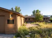 A ranch home's wide wood-sided facade with a blank modern address plaque mounted beside the garage