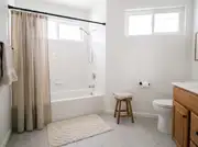 Oatmeal linen shower curtain on a matte black rod, pulled open over a white tiled tub-shower