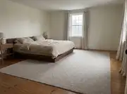Oversized low-pile wool rug sliding under a dark wood platform bed on a wide-plank pine floor