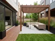 Modern courtyard with a wooden pergola over a wicker seating set with beige cushions, tiled paving, planters, and a lawn
