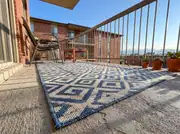Low view of a blue and cream geometric outdoor rug laid over bare concrete with stacking chairs and succulents
