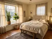 A tall snake plant and a faux fiddle-leaf fig in woven baskets beside a sunlit window and a neutrally dressed bed