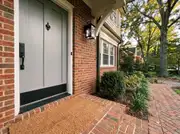 Gray front door with a matte black handle set, kickplate and knocker above a coir doormat on a brick step