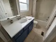 Navy vanity with a resurfaced white stone-look countertop, an oval sink, and a brushed nickel faucet