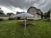 White pop-up canopy staked to the lawn over a food table and folding chairs under a stormy sky