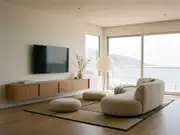 Minimalist living room with a wall-mounted TV above a low wooden media console, floor cushions, and a wide water-view window