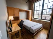 Small loft bedroom with a Murphy wall bed folded down beside a desk and office chair