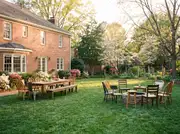Brick-house backyard with a long dining table and bench in one zone and a ring of mixed chairs around a fire pit in another